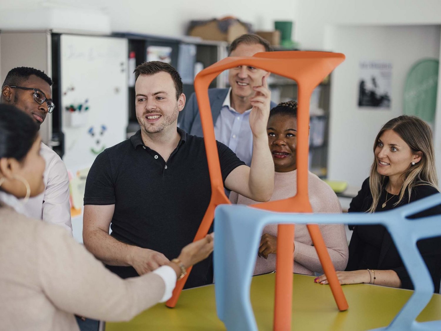 Eine Gruppe steht um einen Tisch herum, auf welchem Figuren positioniert worden sind. Einer der Personen erklärt, die restlichen Personen hören zu.