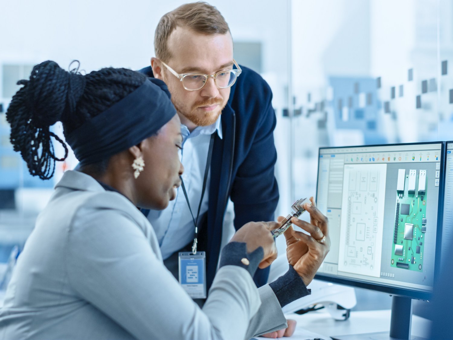 Zwei Personen vergleichen eine Platine mit 3D-Daten am Monitor.