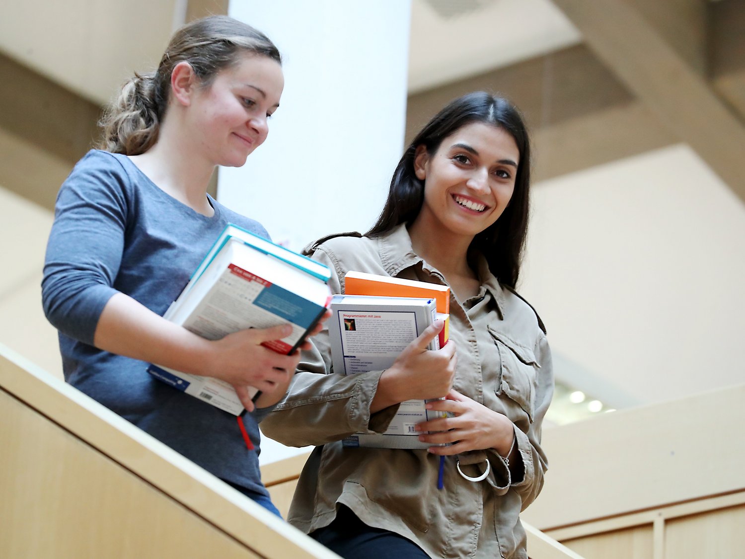 Zwei Personen haben Bücher in den Händen und gehen eine Treppe runter.