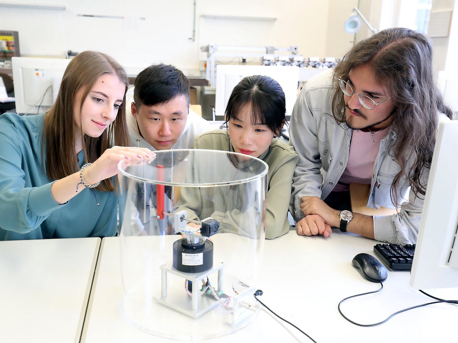 Vier Personen befinden sich im Physiklabor und beobachten einem Versuch.