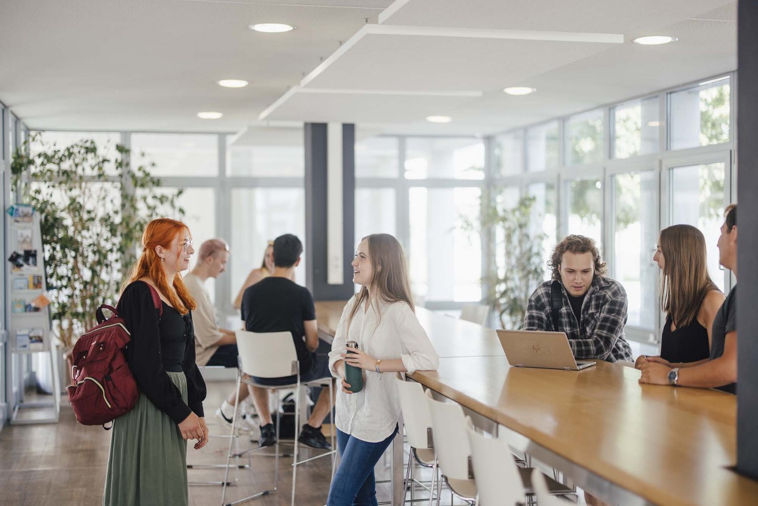 Studierende unterhalten sich an den Hochtischen bei der Cafeteria