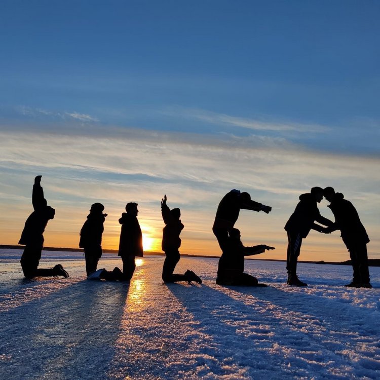 Personen performen einen Schriftzug bei Sonnenuntergang im Schnee.