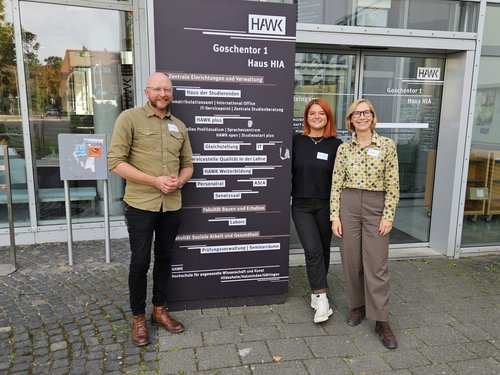 3 Personen stehten vor einem Schild der HAWK