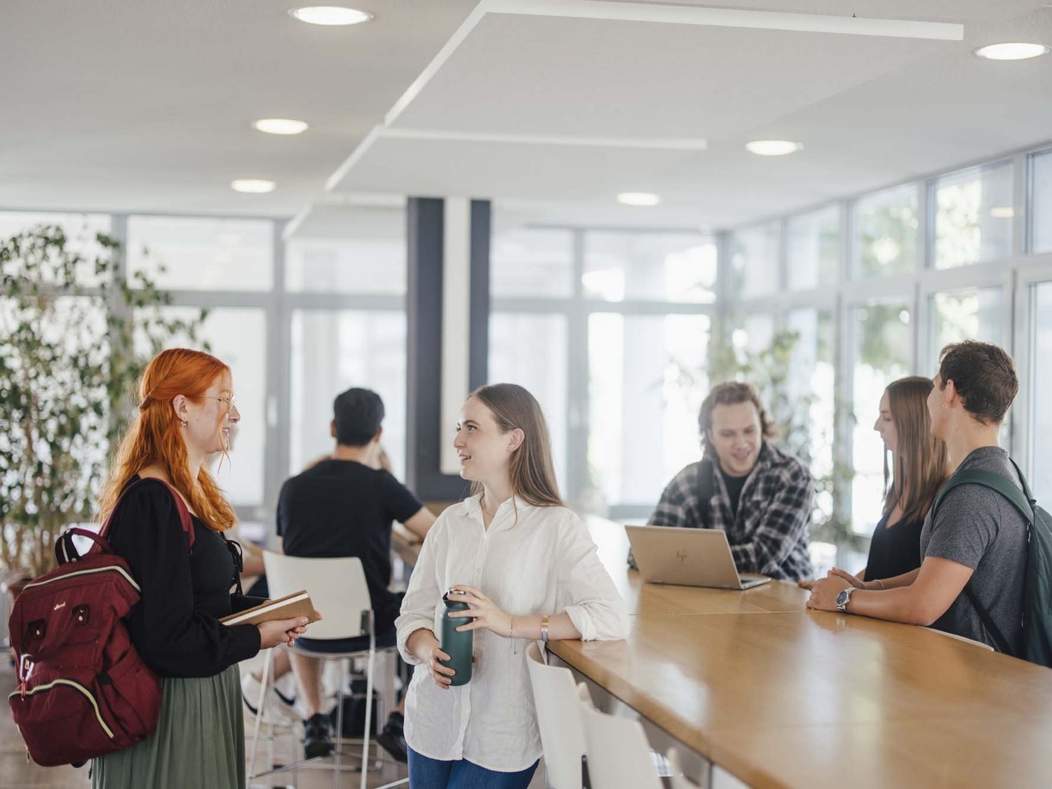 Studierende unterhalten sich an den Hochtischen bei der Cafeteria