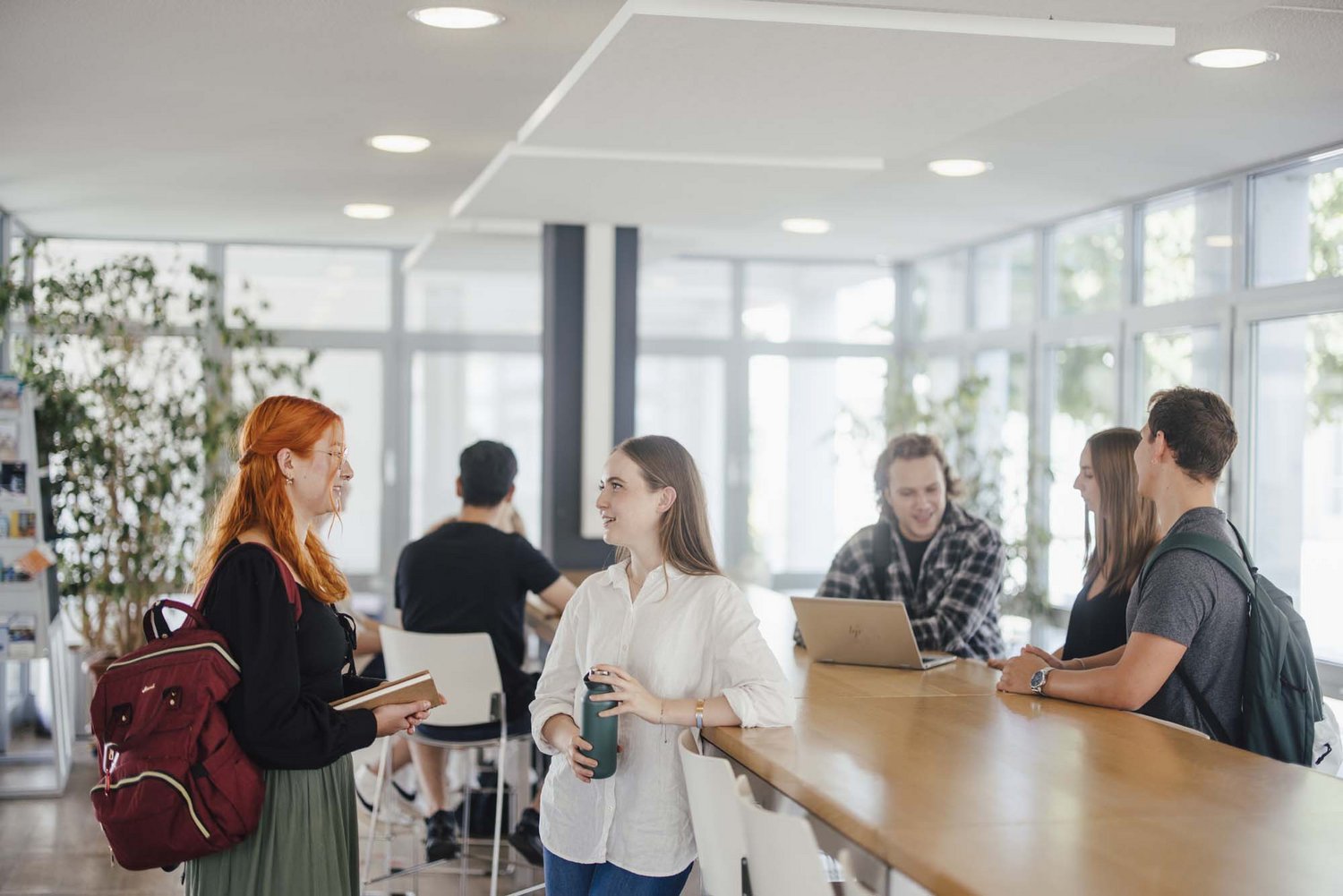 Studierende unterhalten sich an den Hochtischen bei der Cafeteria