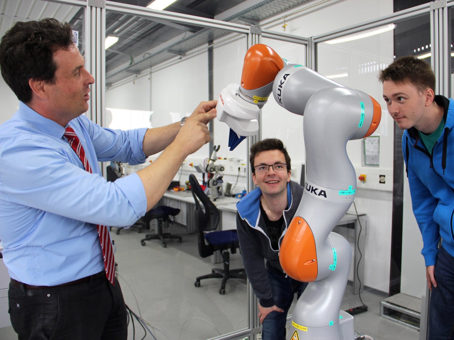 Ein Dozierender erklärt zwei Studierenden einen Roboterarm.